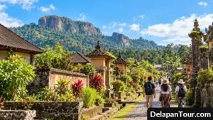 Jalur batu di desa wisata Bali dengan rumah tradisional, taman hijau, dan perbukitan berbatu yang rimbun.